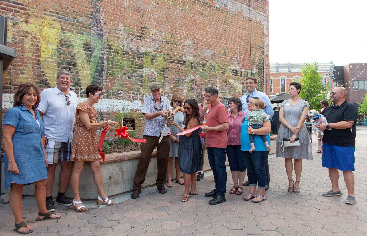 People cut a ribbon in front of garden in a brick plaza.