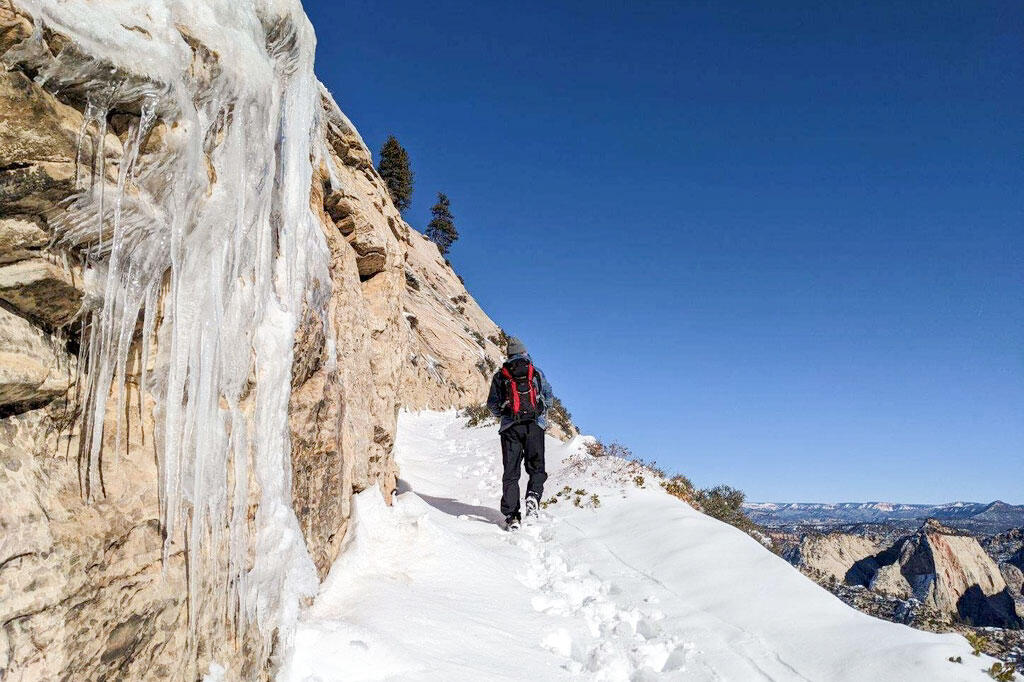 A man hikes through snow alongside a cliff.