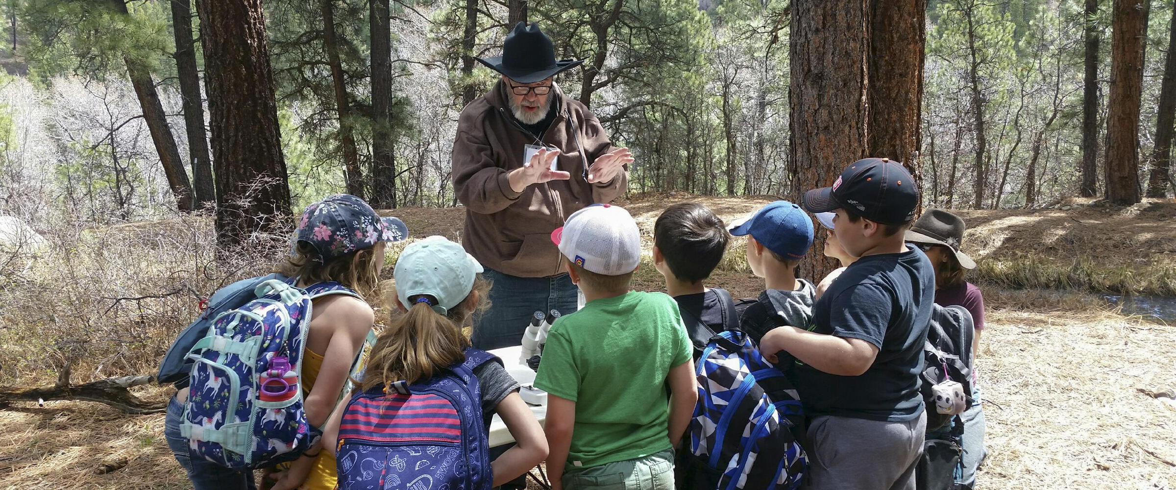 A man teaches a group of children about nature in a forest.