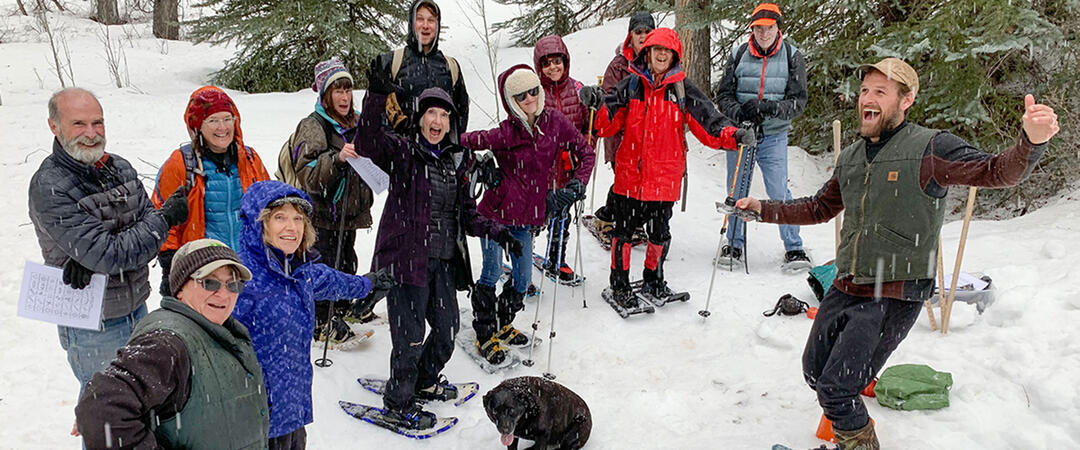 A group of adults posing in snowshoes in a snowy forest.